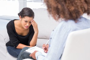 Woman crying on sofa during therapy session while therapist is t