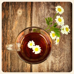 Glass cup of camomile tea with camomile flowers, on vintage wood