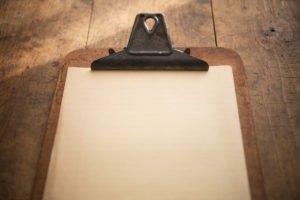 An vintage clipboard on a old wooden table, with blank old white