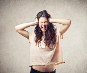 A woman with long hair stands against a gray background, pulling her hair and screaming in frustration. As someone exploring CRPS resources online, she seeks effective coping skills for chronic pain to manage her stress.