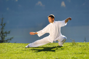 Dressed in white martial arts attire, a person gracefully performs a Tai Chi pose on a grassy area. With elegance and focus, this practice can be one of the coping strategies for chronic pain, offering both physical and mental relief amidst life's challenges.