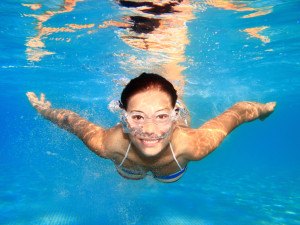 Woman swimming underwater in pool smiling. Young female swimmer