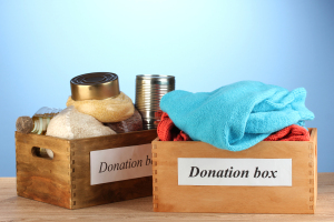 Two wooden boxes labeled "Donation Box" hold canned goods and clothing on a wooden surface against a blue background, offering resources for understanding chronic pain through community giving.