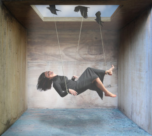 A woman in a black dress swings gracefully, suspended by strings held by birds inside a wooden box with an open ceiling revealing the sky—a serene escape that mirrors self-help resources for chronic illness, offering hope and strategies for coping.