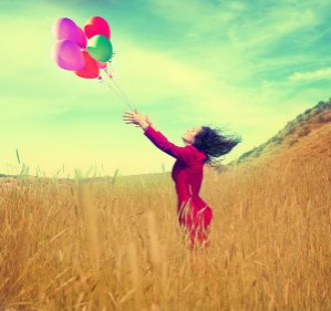 a girl walking in a field letting go of a bunch of balloons done with a vintage retro instagram filter effect