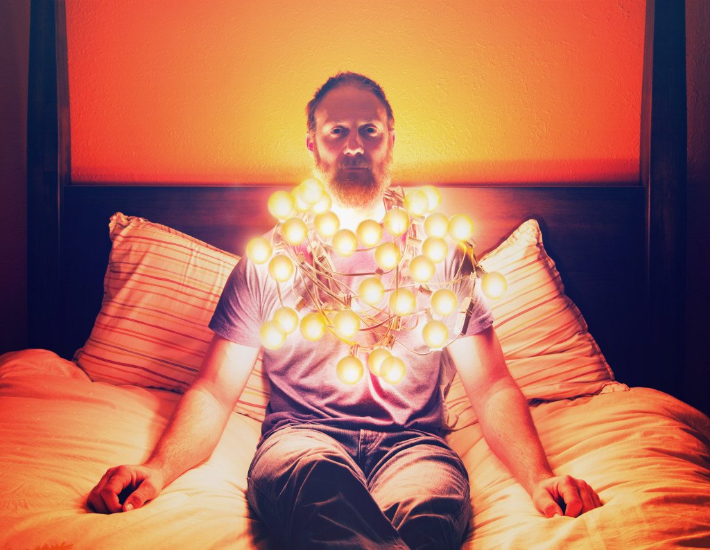 a man draped in christmas lights sitting on a bed looking depres